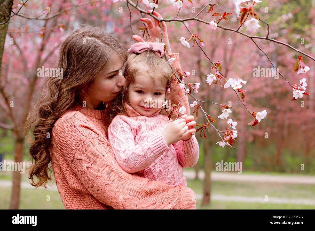 madre e bambina in abiti rosa, abbraccia il parco con sakura rosa fiorente. Foto Stock