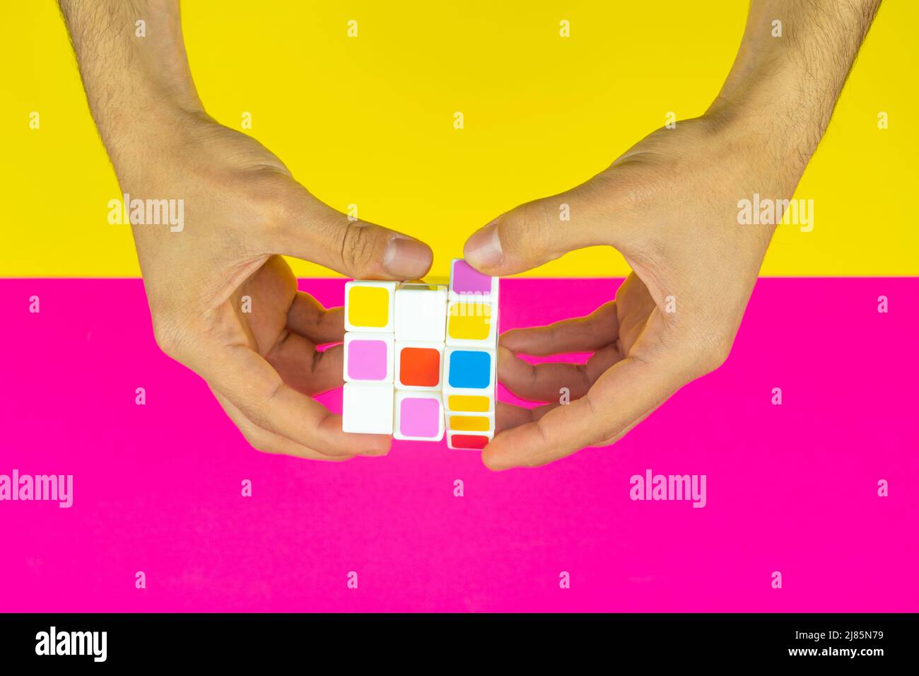 Mani che giocano con cubo colorato con sfondo rosa e giallo, intelligenza e gioco di cervello, vista dall'alto, vista dall'alto di un cubo Foto Stock