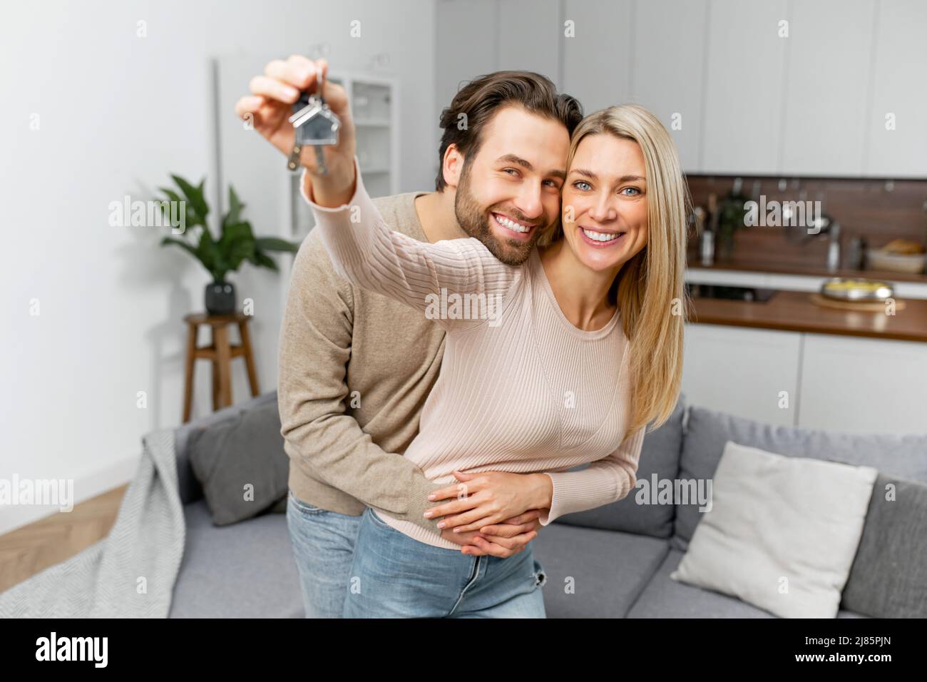 Felice coppia di famiglia caucasica che mostra nuove chiavi della casa alla macchina fotografica mentre posa in casa. Casa propria, proprietà immobiliare e alloggi. Ipoteca e acquisto di appartamento Foto Stock