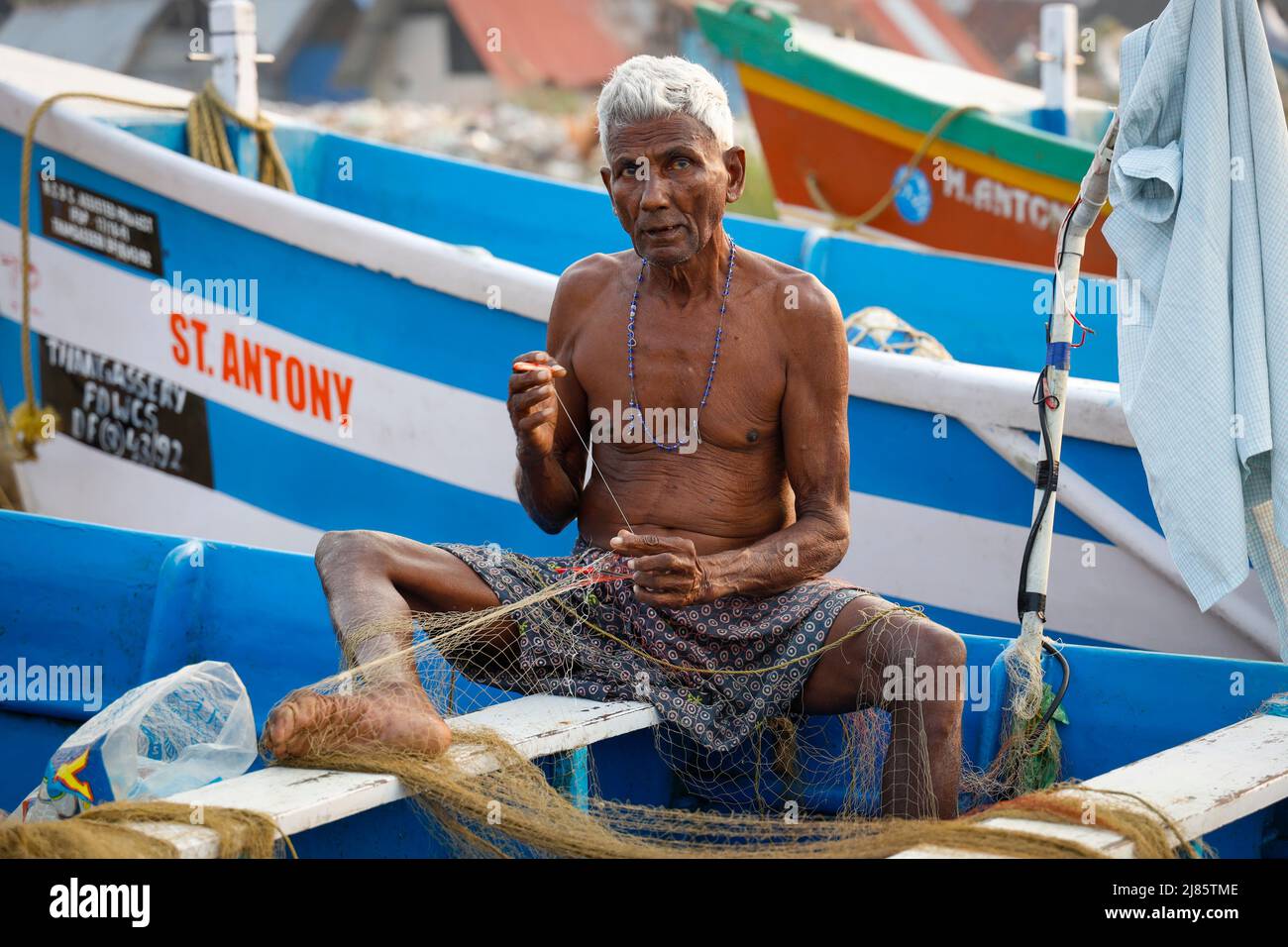 Ritratto di vecchio pescatore che menda la sua rete da pesca, Tangassery, Kerala, India. Foto Stock