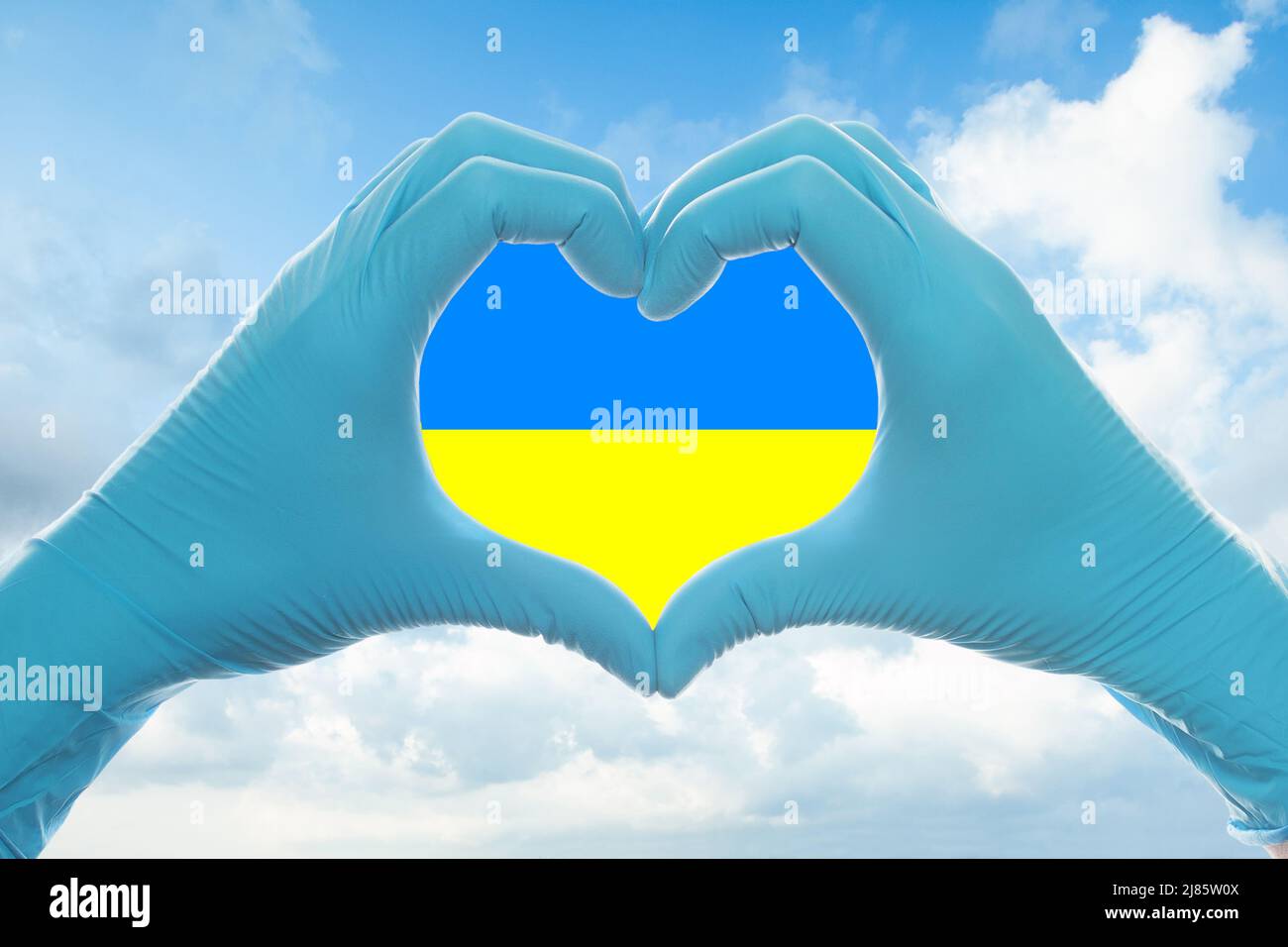 Mani in guanti medico che mostrano il cuore contro le nuvole del cielo Foto Stock
