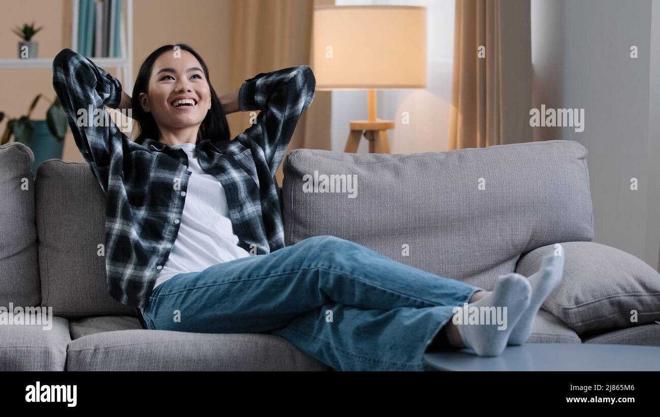 Calma felice donna asiatica stanca casalinga che riposa su morbido divano che tiene le mani dietro la testa coreana donna rilassarsi sul comodo divano napping sensazione di stress Foto Stock