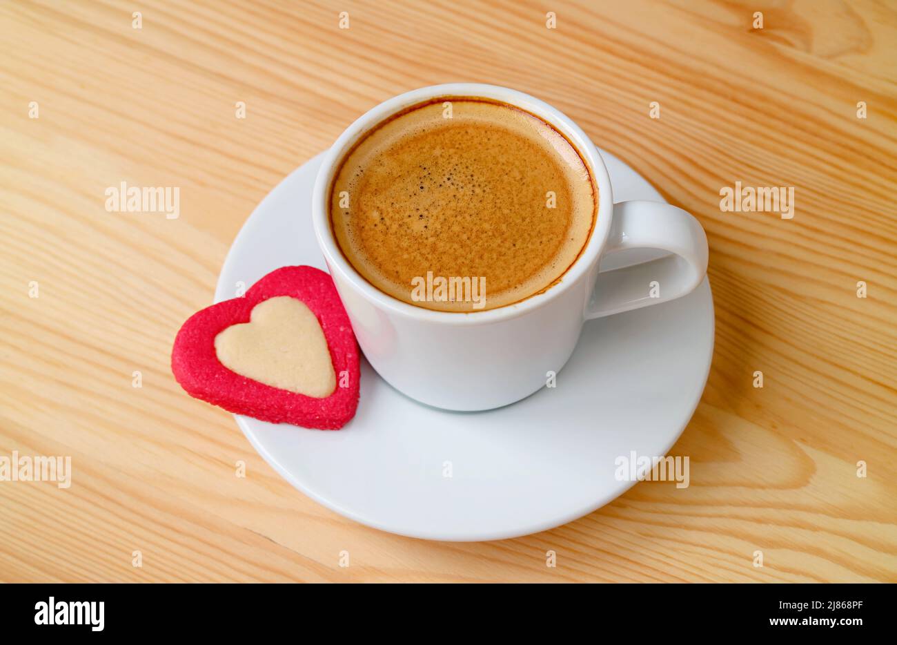 Una tazza di caffè caldo con un biscotto a forma di cuore su sfondo di legno Foto Stock