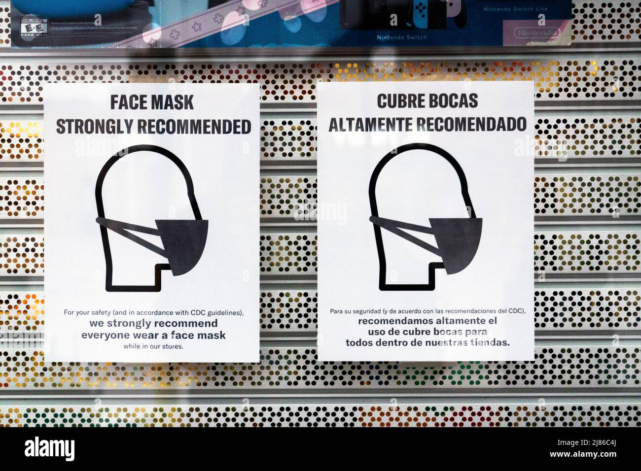 Maschere bilingui segni fuori di un negozio in Astoria, Queens, New York incoraggiando maschere anche pensato che non sono obbligatori. Foto Stock
