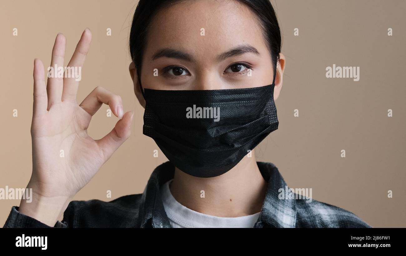 Asian korean japanese chinese donna ritratto femmina viso ragazza indossare nero viso medico maschera protettiva covid pandemic regole mostrando ok gesto bene Foto Stock