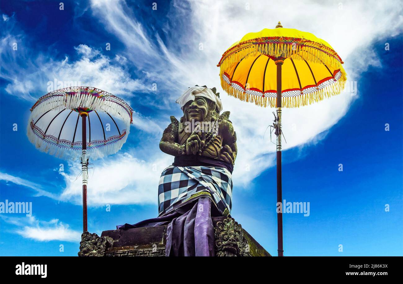 Figura in pietra del signore shiva, mitologico balinese indù, tra due tradizionali ombrelli cerimoniali (Tedung), nuvole bianche di cielo blu - Bali, Ubud Foto Stock