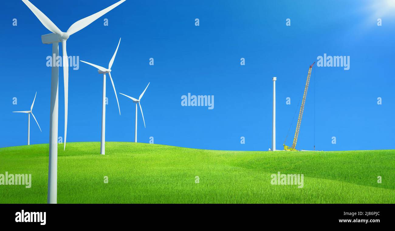 Windfarm in un campo di erba verde con gru da costruzione che installa la nuova turbina eolica contro il cielo blu Foto Stock