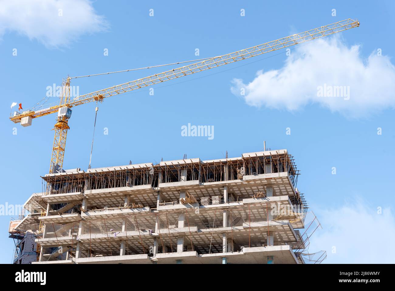 Gru da costruzione sullo sfondo di un edificio incompiuto e di un cielo blu con nuvole. Foto Stock