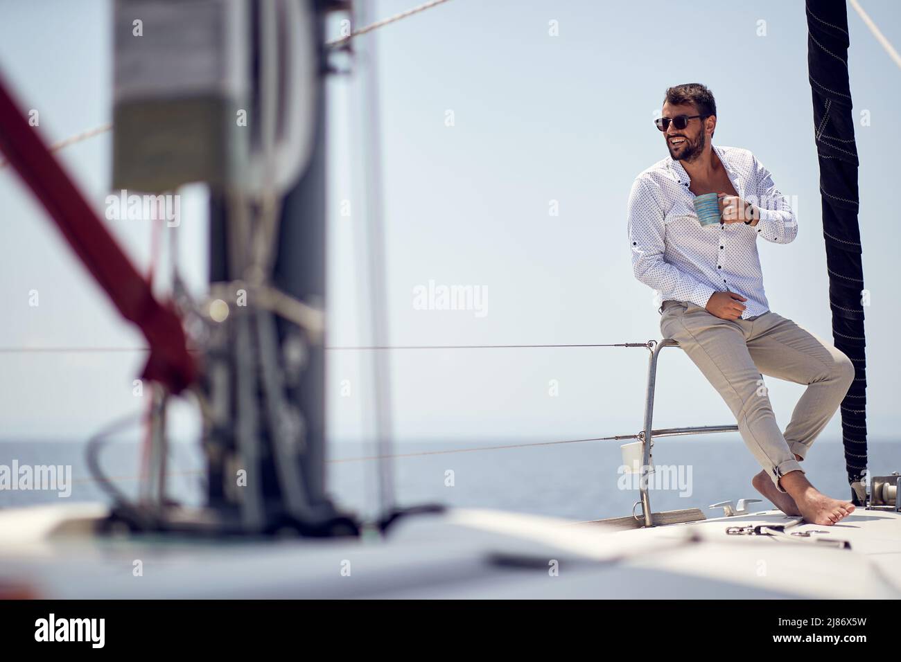 Un giovane bel modello maschio a piedi nudi è di buon umore mentre si gode una foto di scatto su uno yacht in una bella giornata di sole sul mare. Estate, mare Foto Stock