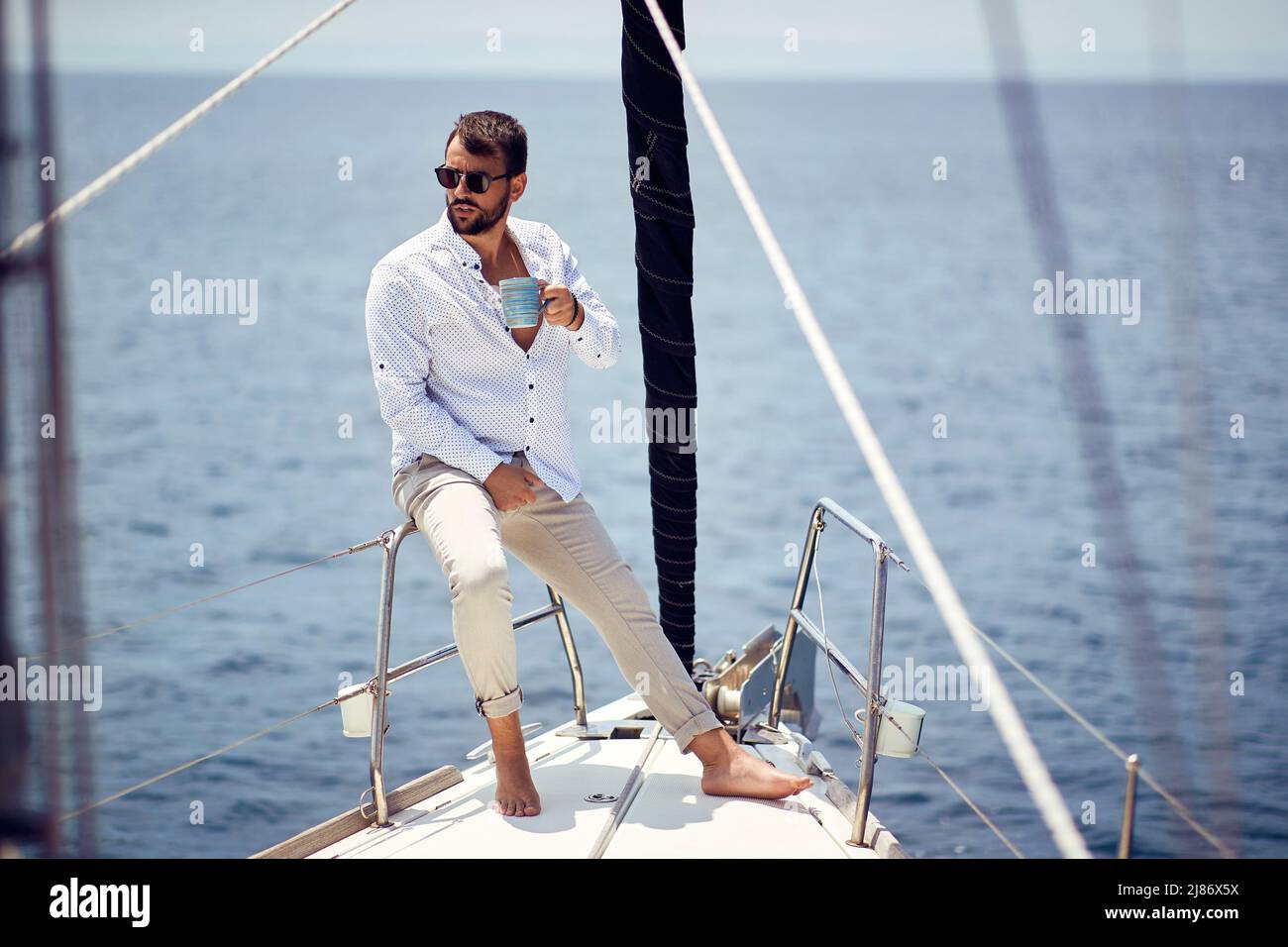 Uomo informale e attraente che naviga da solo sullo yacht; concetto di stile di vita lussuoso Foto Stock
