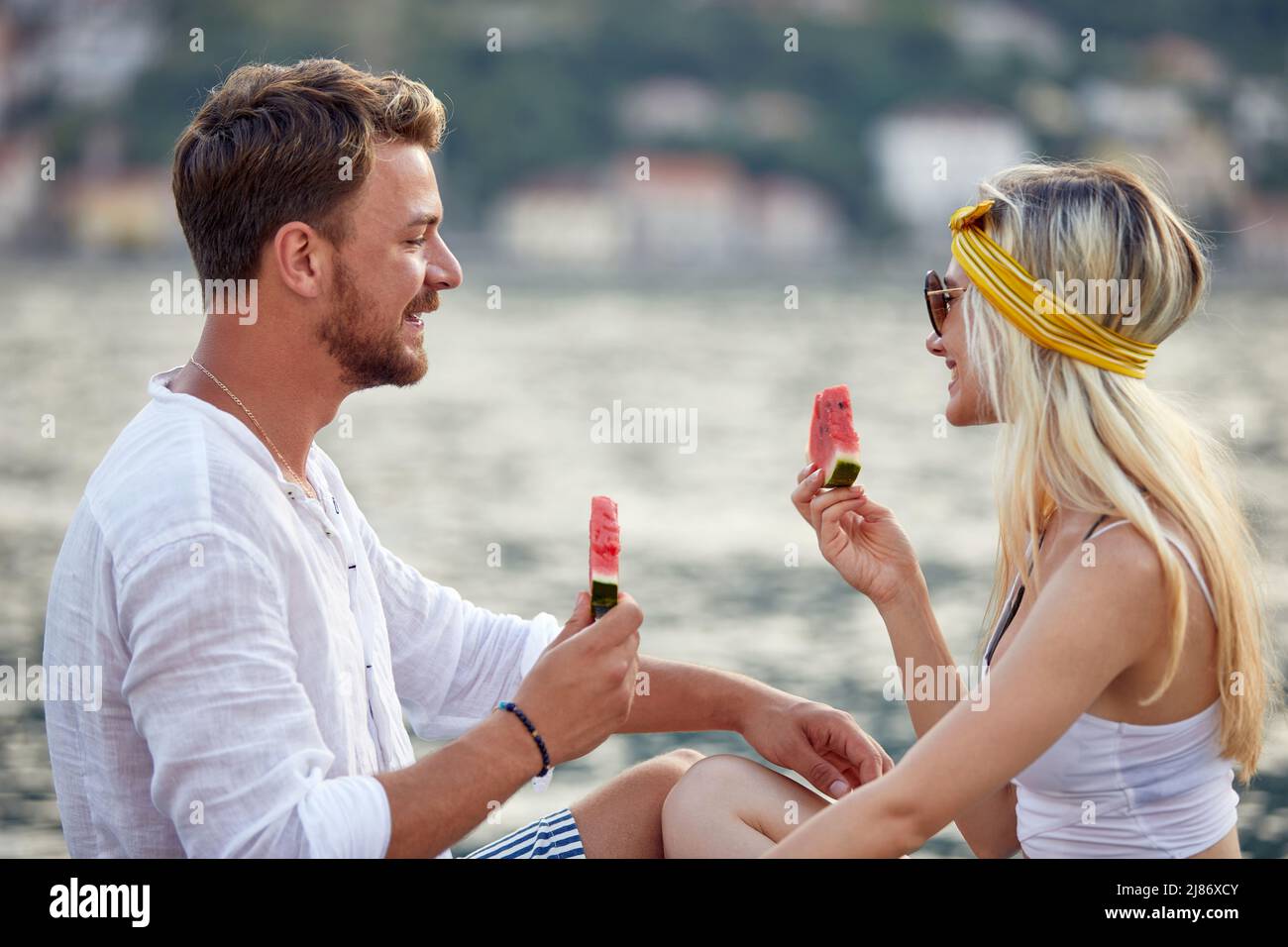 Coppia gioiosa in data in estate dal mare al molo, mangiare cocomero. Viaggi, amore, divertimento, convivenza, stile di vita. Foto Stock