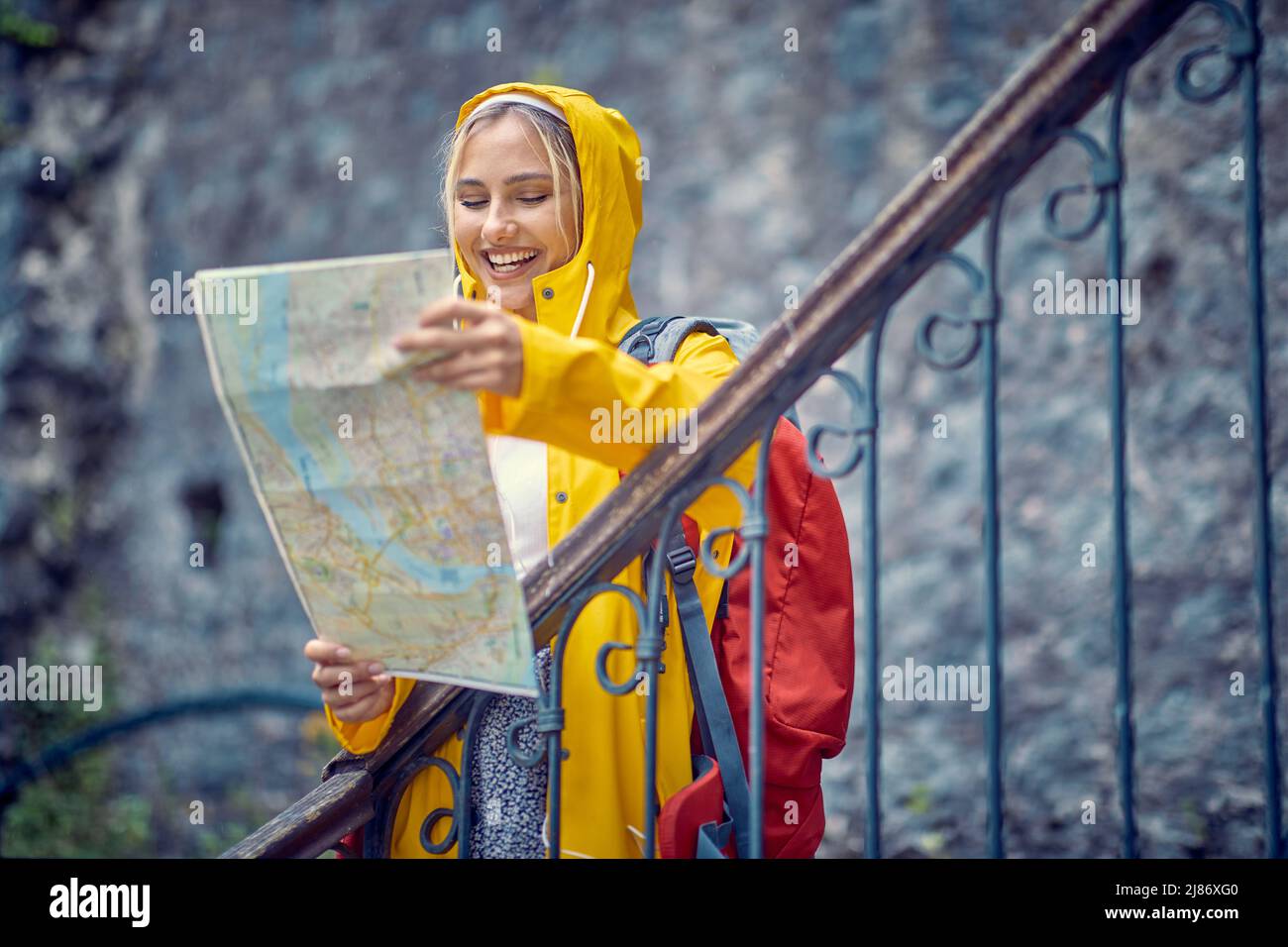 Viaggiatore sorridente ragazza con mappa in vacanza. Felice femmina in giallo impermeabile e mappa godendo giorno di pioggia Foto Stock