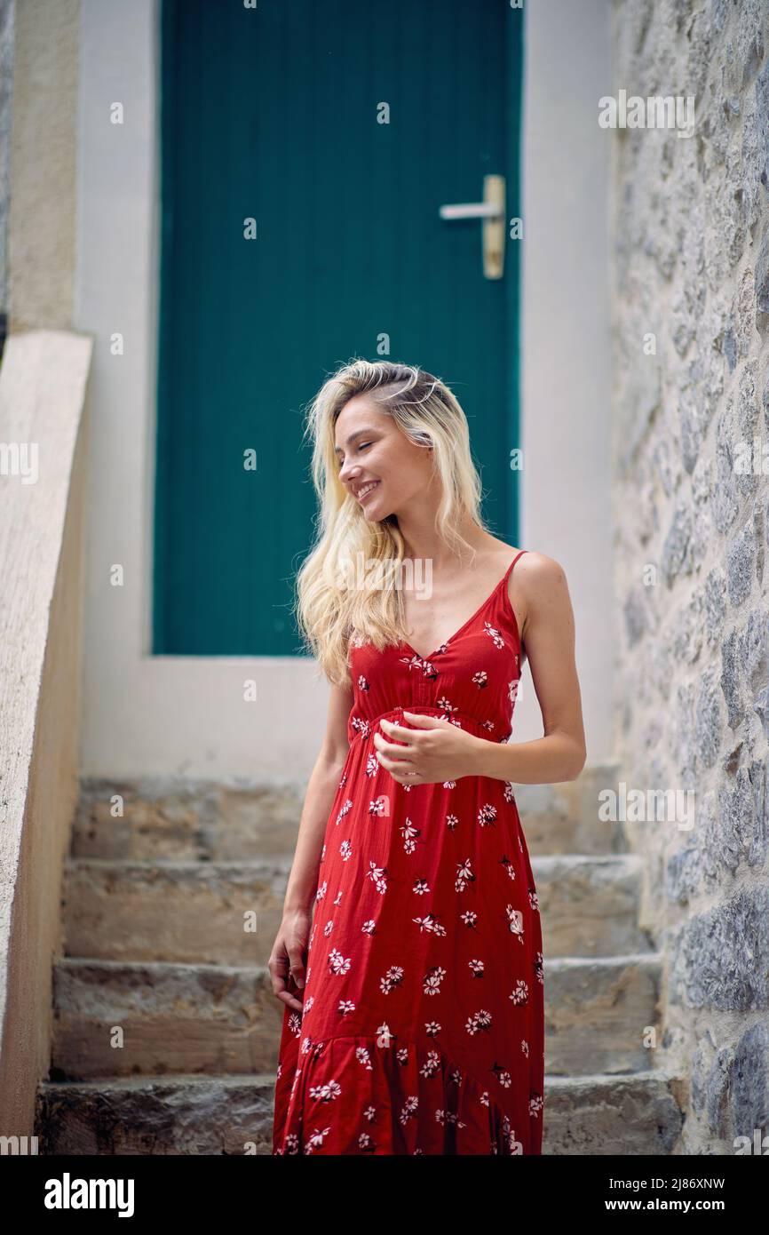 Una giovane ragazza bella in un abito rosso è pronta per una passeggiata nella città vecchia in una bella giornata durante una vacanza sul mare. Vacanze, mare, turismo Foto Stock