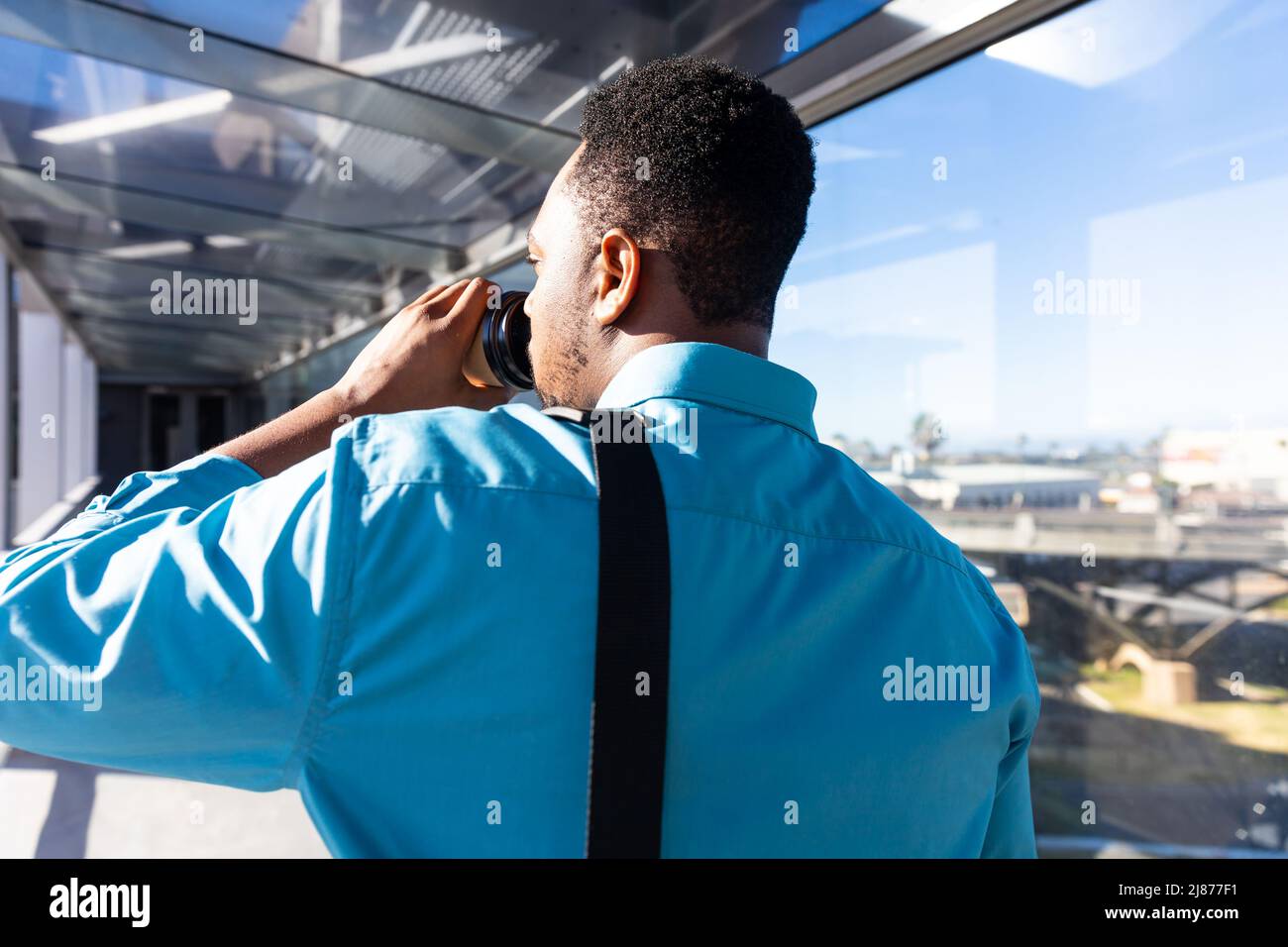 Vista posteriore del viaggiatore d'affari afroamericano che beve caffè al corridoio dell'aeroporto in giorno di sole Foto Stock