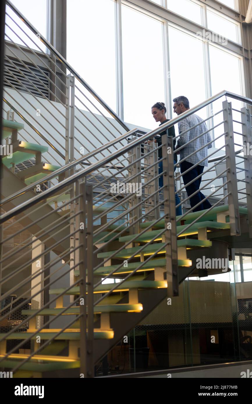 Vista ad angolo basso dei colleghi caucasici che progettano mentre si sale su una scala nel moderno ambiente di lavoro Foto Stock