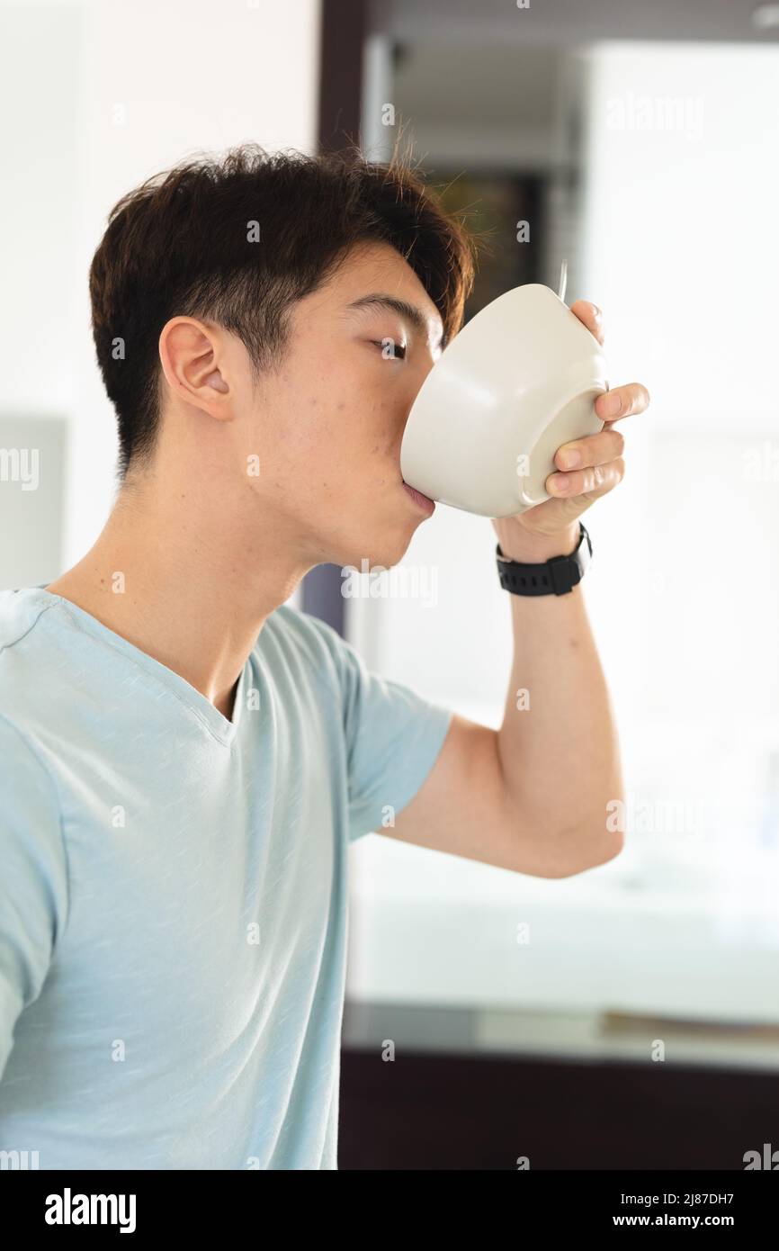 Primo piano del ragazzo asiatico con t-shirt blu che beve zuppa con ciotola mentre si trova a casa Foto Stock