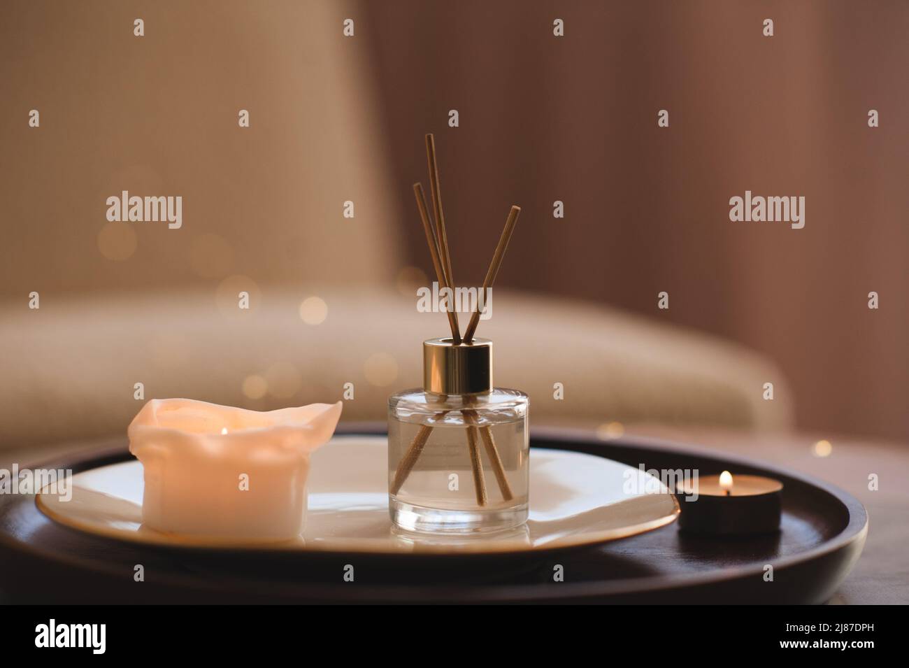 Profumo liquido per la casa in bottiglia di vetro con bastoncini di bambù con candela profumata sul piatto su vassoio di legno sul tavolino da caffè in camera da letto primo piano. Foto Stock