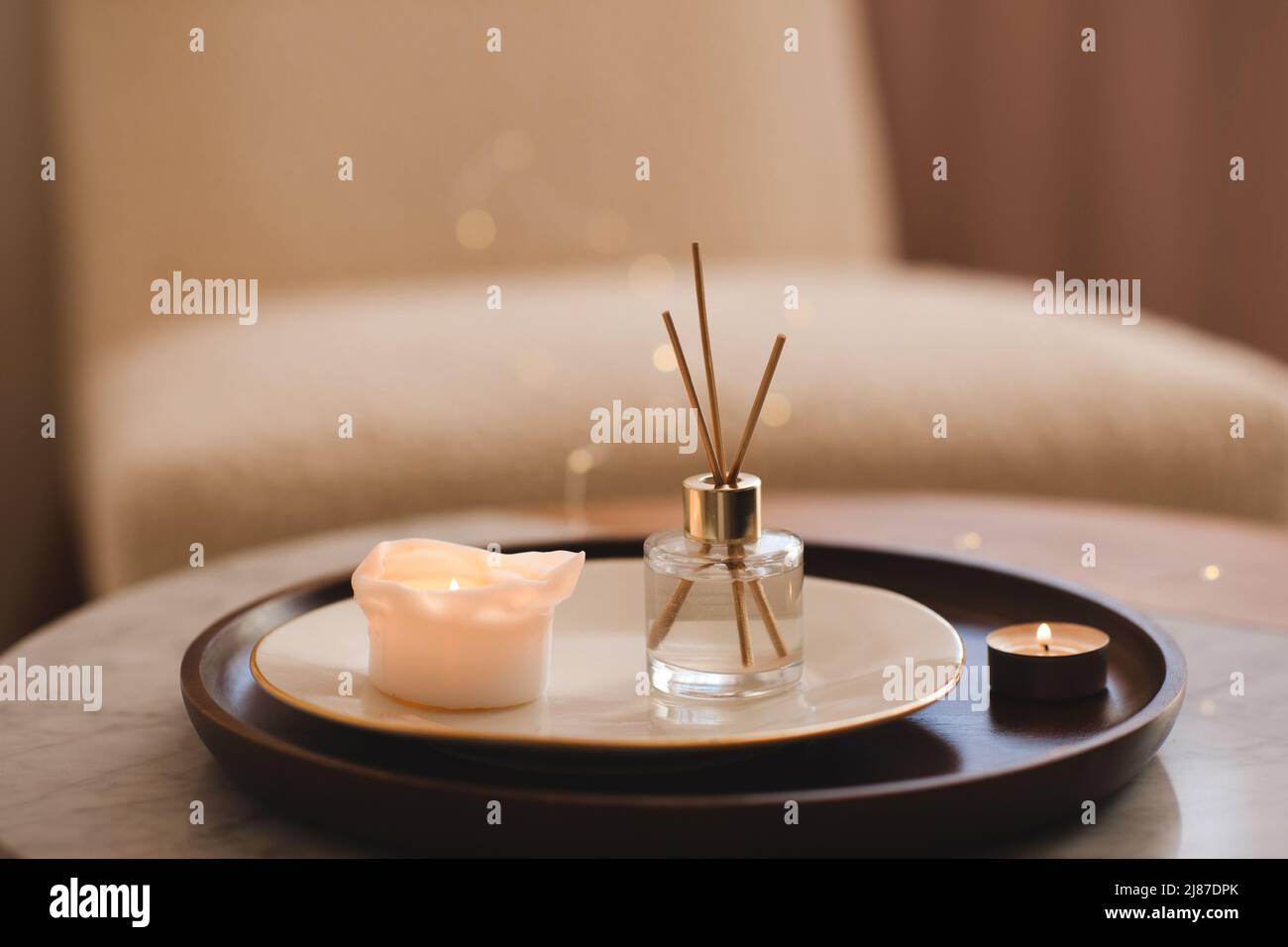 Profumo liquido per la casa in bottiglia di vetro con bastoncini di bambù con candela profumata sul piatto su vassoio di legno sul tavolino da caffè in camera da letto primo piano. Foto Stock