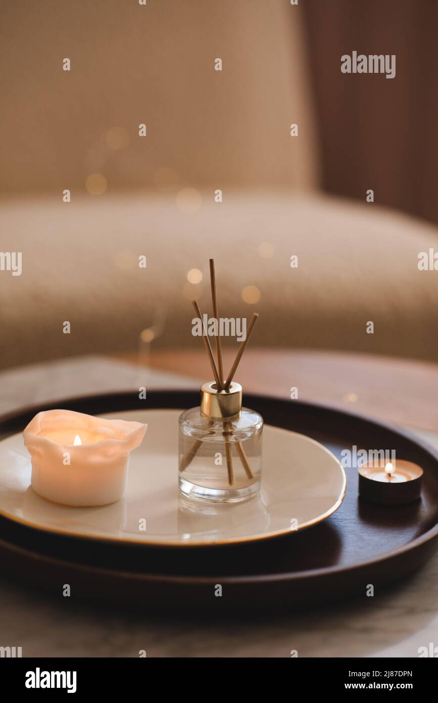 Profumo liquido per la casa in bottiglia di vetro con bastoncini di bambù con candela profumata sul piatto su vassoio di legno sul tavolino da caffè in camera da letto primo piano. Foto Stock