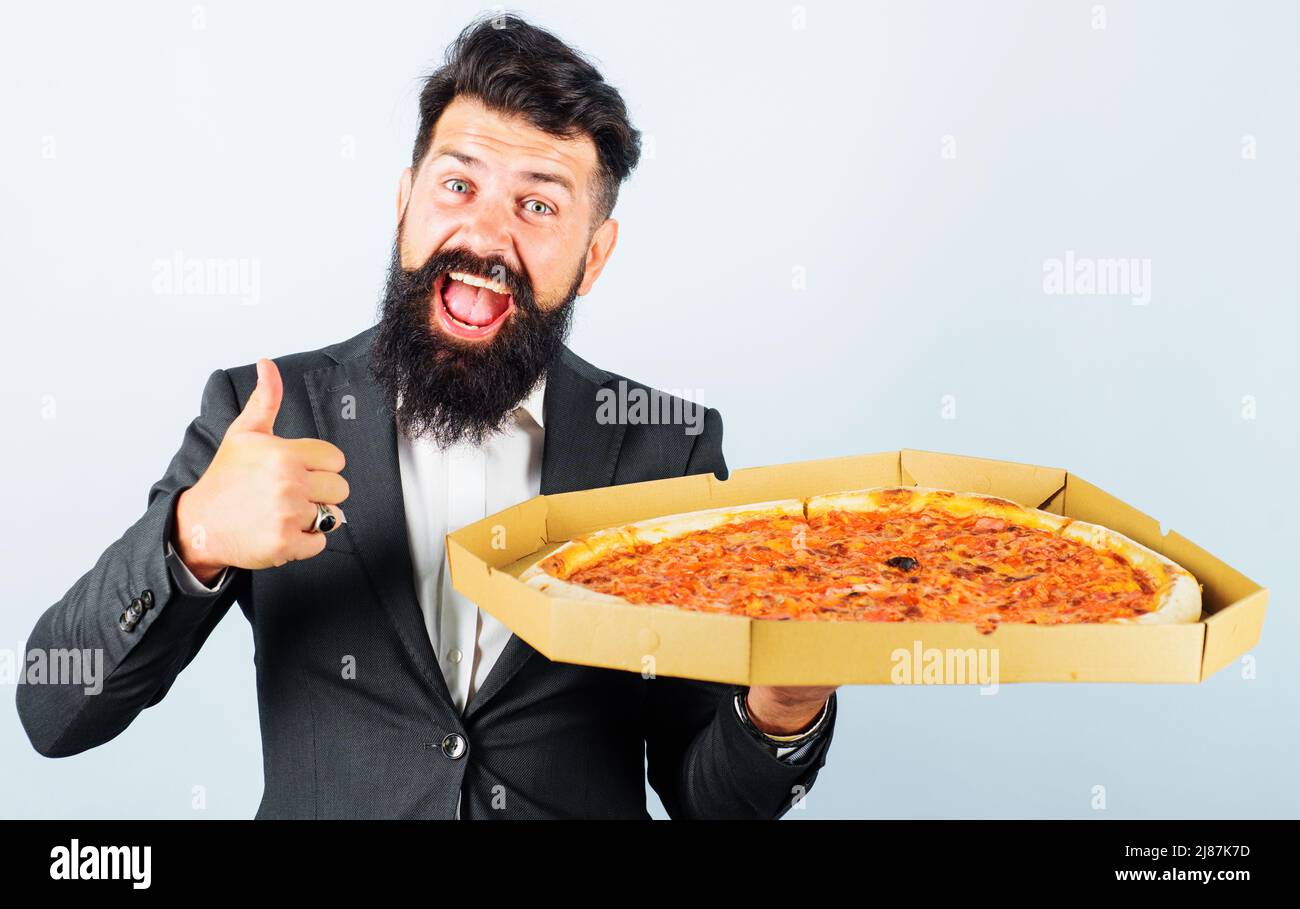 Felice uomo bearded in vestito con pizza mostra pollice in su. Pranzo di lavoro. Cucina italiana. Consegna pizza Foto Stock