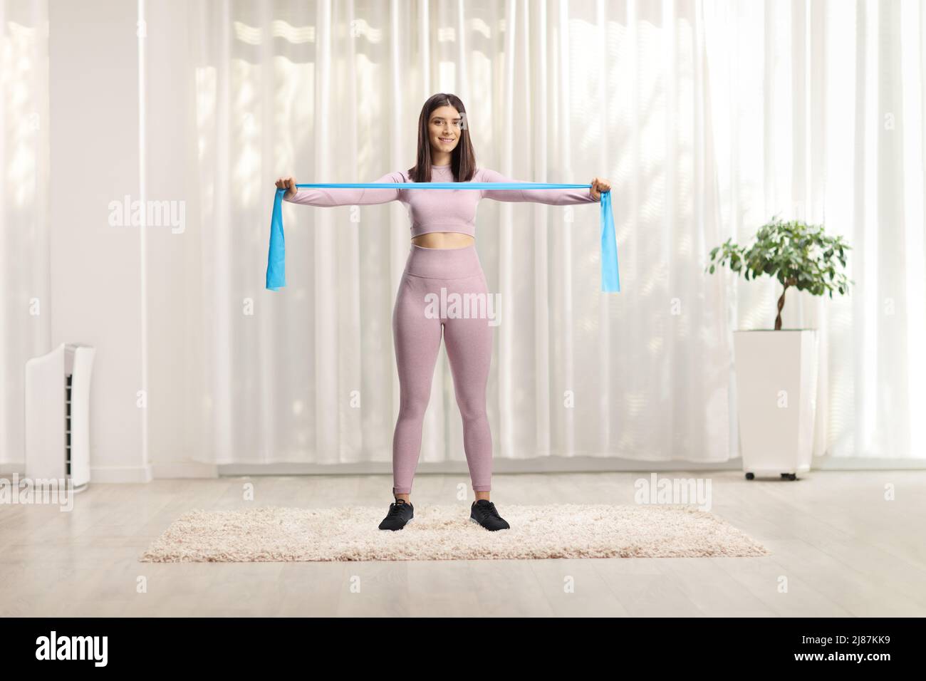 Ritratto a tutta lunghezza di una giovane donna in leggings e crop top esercitarsi con un elastico elastico elastico fascia in gomma a casa Foto Stock