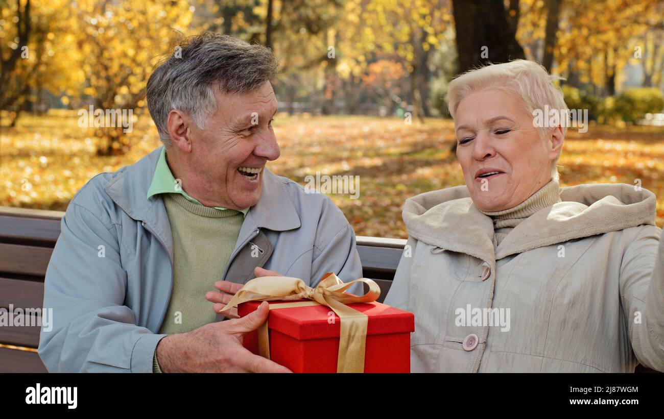 L'uomo maturo dà il regalo alla moglie amata sul compleanno la donna anziana ridono felicemente la coppia sposata positiva che celebra la sorpresa inaspettata di anniversario Foto Stock