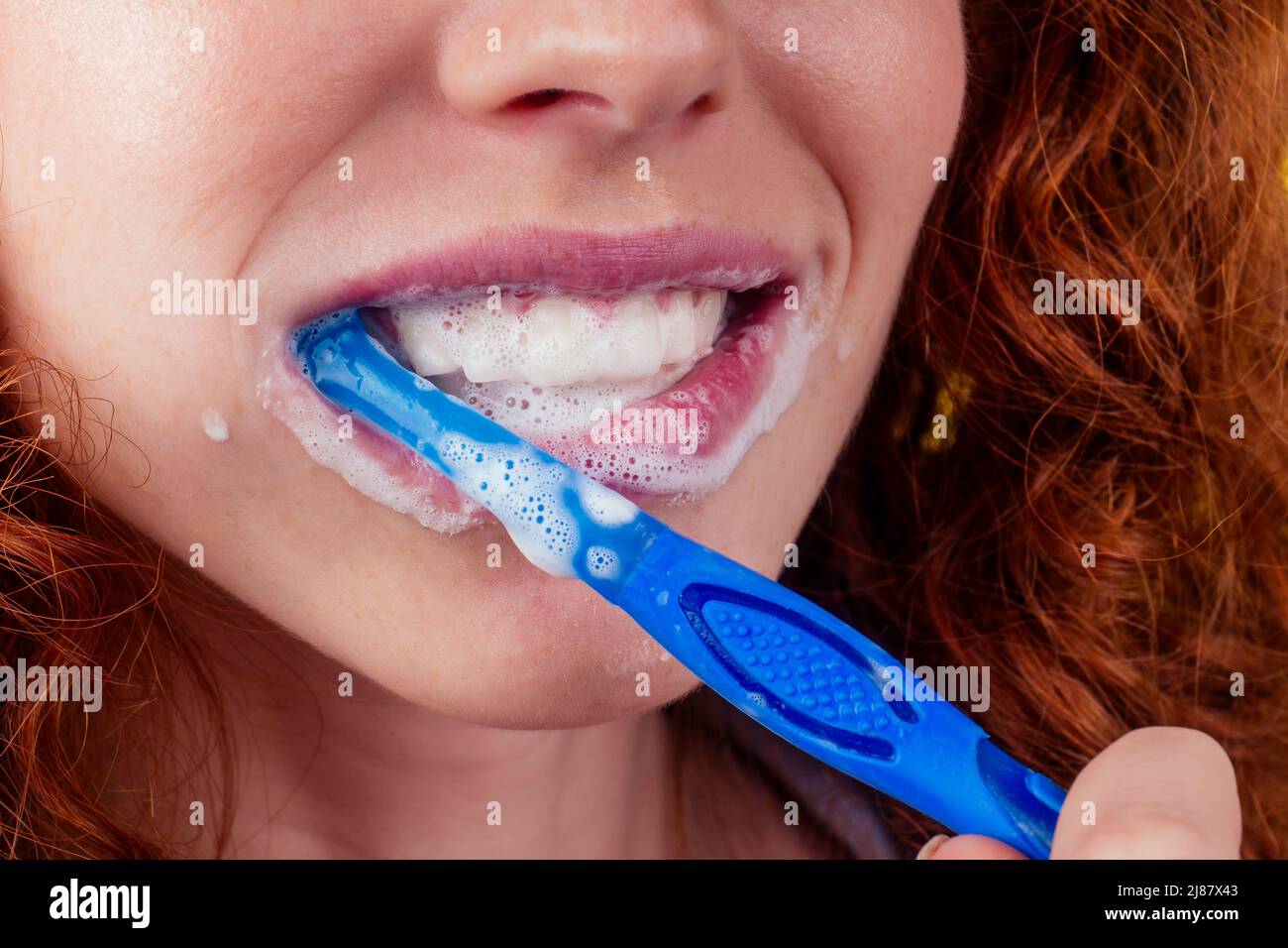 zenzero rosso donna spazzolando i denti con dentifricio pasta eco su sfondo giallo studio Foto Stock