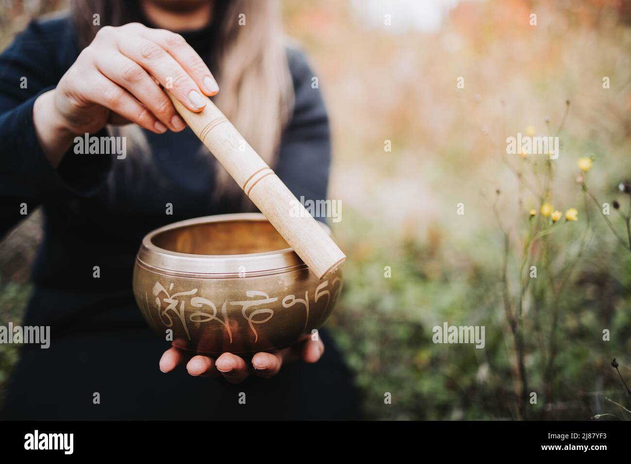 Donna vestita nera fuori tenendo e giocando una ciotola di canto tibetano con un bastone di legno. Messa a fuoco selettiva Foto Stock