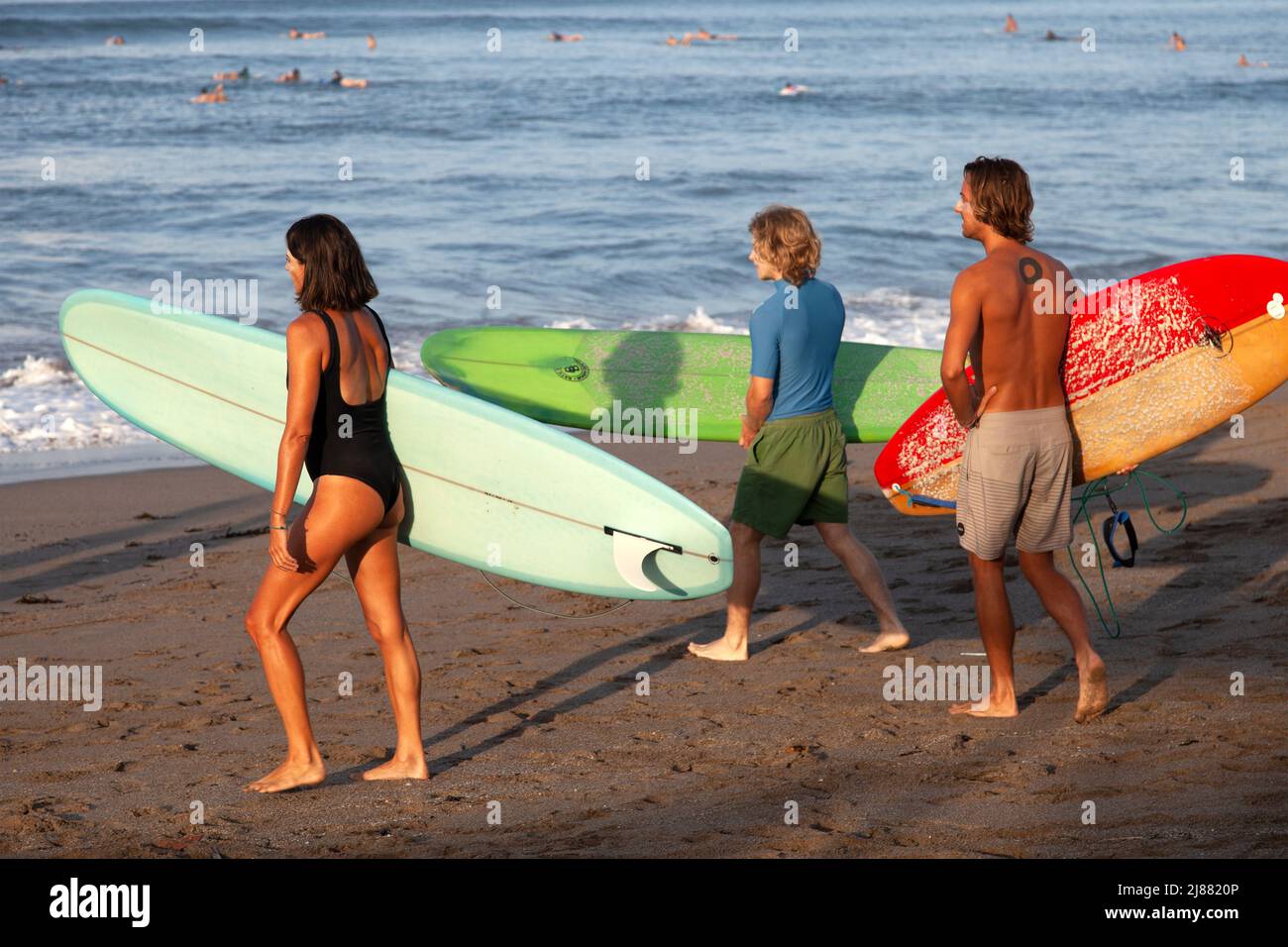 Tre persone, locali e caucasici che camminano verso l'oceano portando tavole da surf alla spiaggia di Batu Bolong a Canggu, Bali, Indonesia. Foto Stock