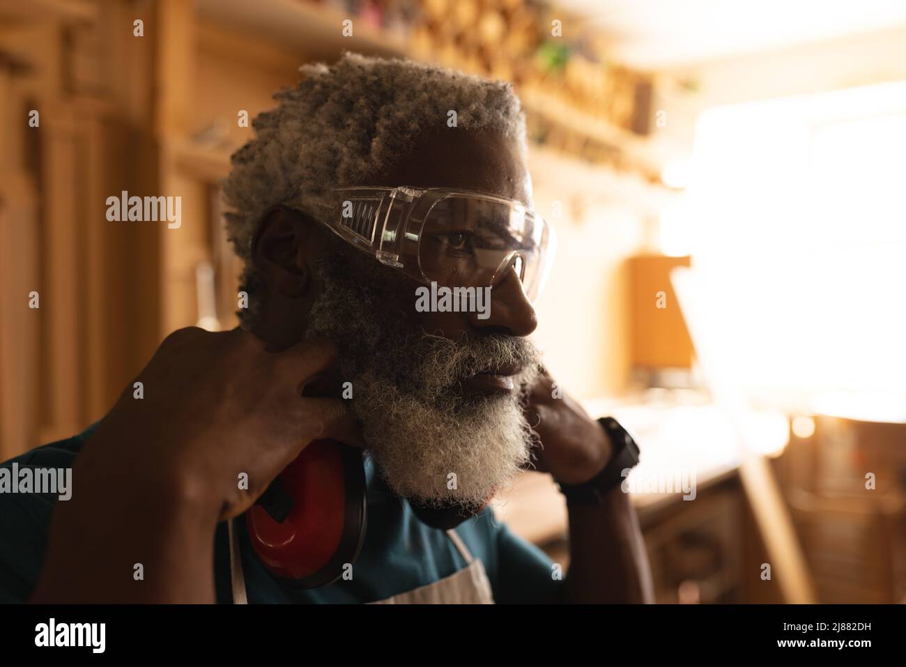 Falegname maturo afroamericano che indossa occhiali protettivi e cuffie in officina Foto Stock