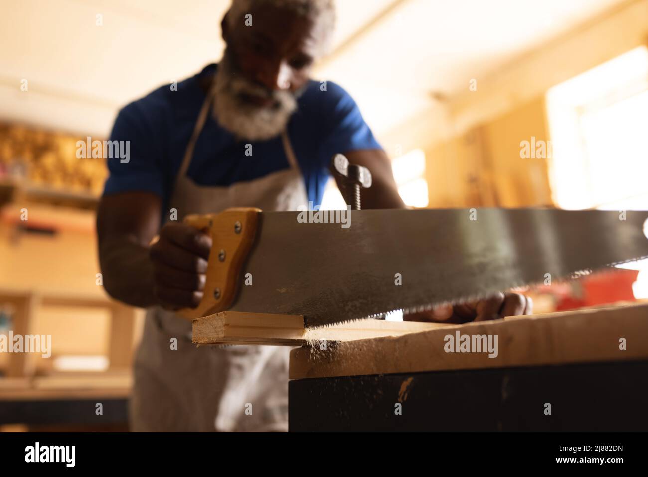 Falegname maturo afroamericano che taglia la tavola con sega al banco da lavoro in officina Foto Stock