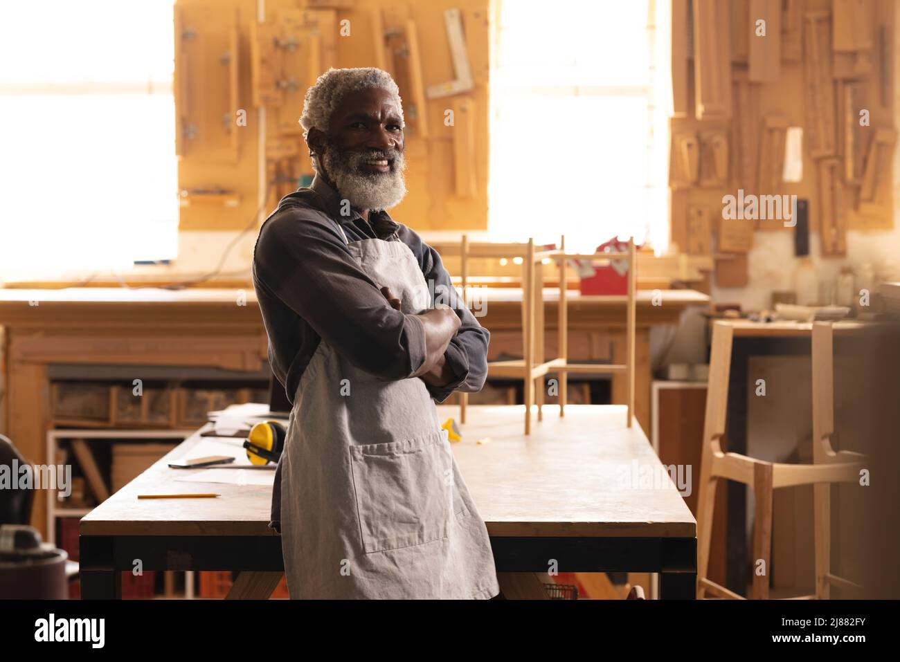 Ritratto di carpentiere afroamericano maturo sorridente in piedi con le braccia incrociate in officina Foto Stock