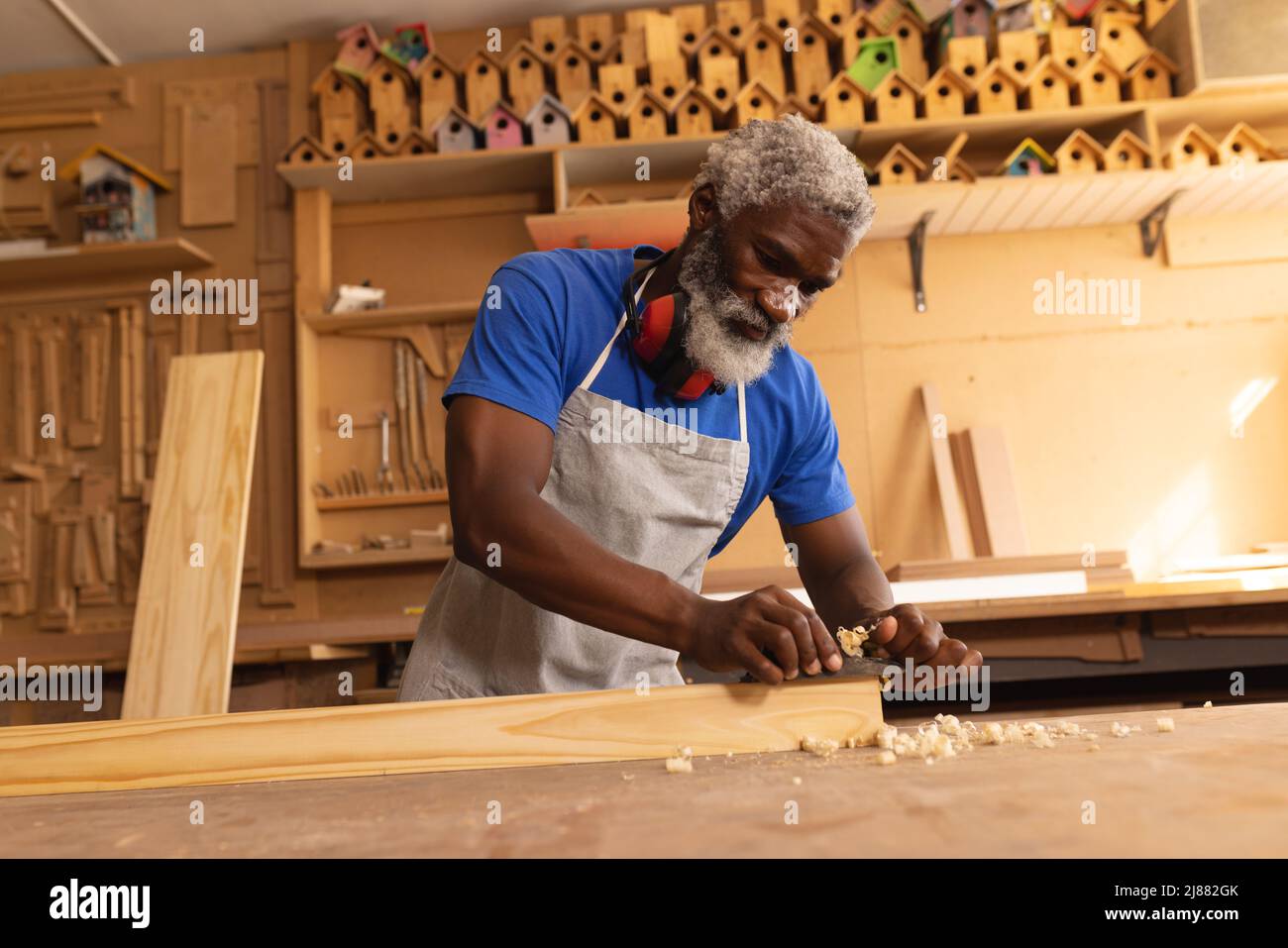 Falegname maturo afroamericano che pianifica la tavola mentre lavora in officina Foto Stock