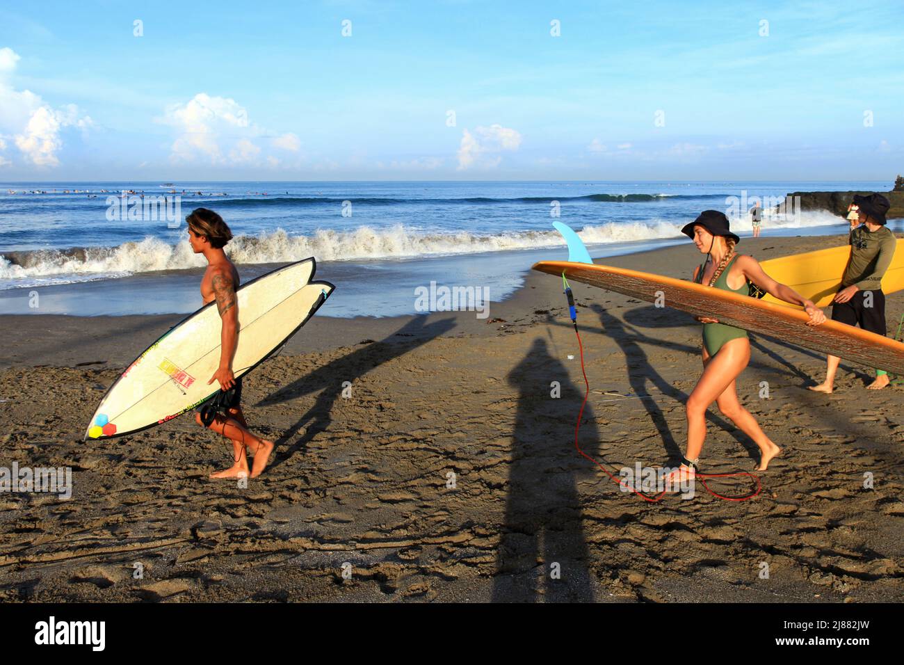 Tre persone, locali e caucasici che camminano verso l'oceano portando tavole da surf alla spiaggia di Batu Bolong a Canggu, Bali, Indonesia. Foto Stock