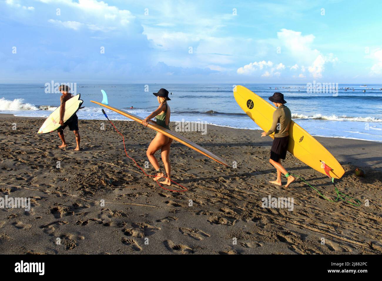 Tre persone, locali e caucasici che camminano verso l'oceano portando tavole da surf alla spiaggia di Batu Bolong a Canggu, Bali, Indonesia. Foto Stock
