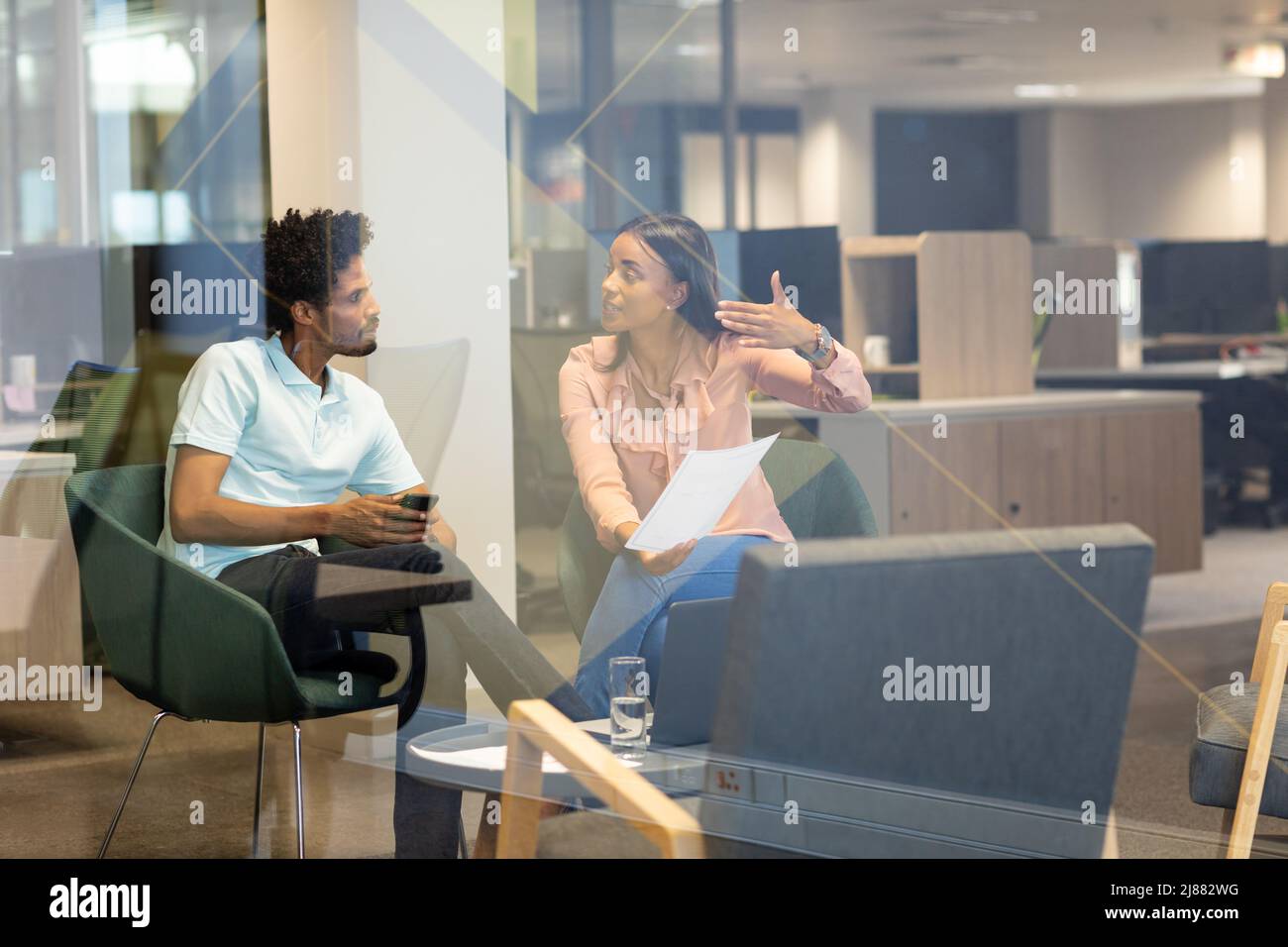 I giovani colleghi biraciali hanno visto attraverso una parete di vetro discutere insieme la strategia nel luogo di lavoro moderno Foto Stock