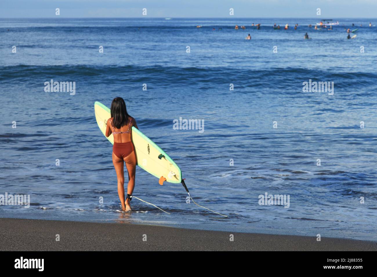 Una giovane donna asiatica indonesiana con lunghi capelli neri che indossa un bikini marrone con una tavola da surf a lunga tavola alla spiaggia di Batu Bolong a Canggu, Bali, Indonesia Foto Stock