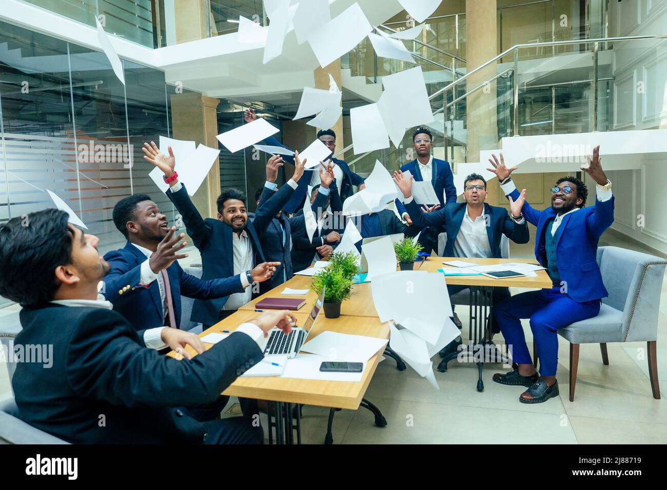 gruppo internazionale di nove persone afro-americane e indiane che si divertono e gettano carta dopo la tempesta di cervello in grande ufficio Foto Stock