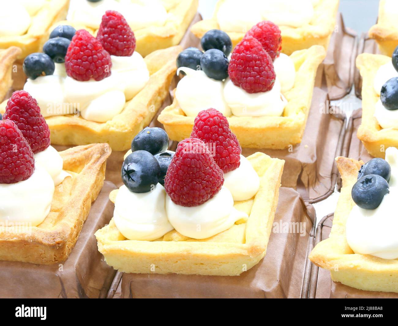 dolci ripieni di panna e molti frutti di bosco in vendita in una pasticceria Foto Stock