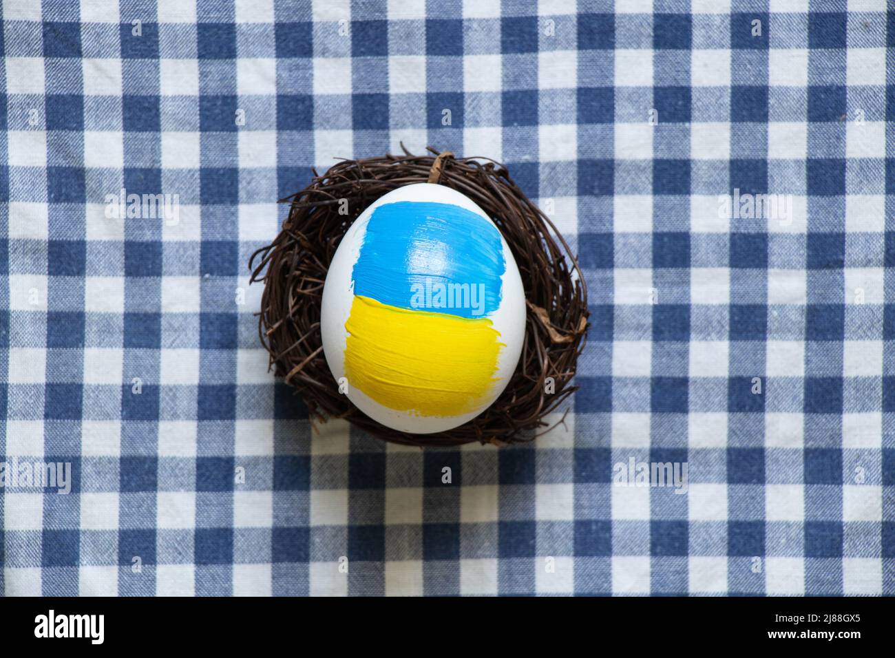 Uovo di pollo bianco con una bandiera dipinta di Ucraina in un cestino di paglia sul tavolo a casa, la cultura e le vacanze 2022 nella guerra in Ucraina Foto Stock