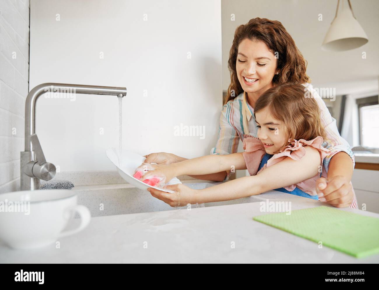bambino cucina piatto casa casalinga lavaggio capretto madre aiutando lavandino gir chore casa acqua famiglia Foto Stock