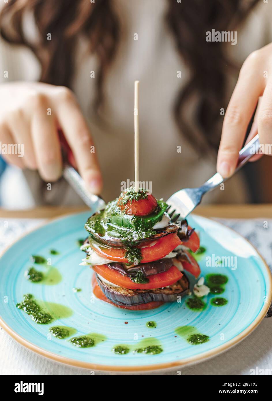 Vista della donna che mangia una melanzana e una timpana di pomodoro su un piatto. Cibo delizioso e salutare al ristorante Foto Stock
