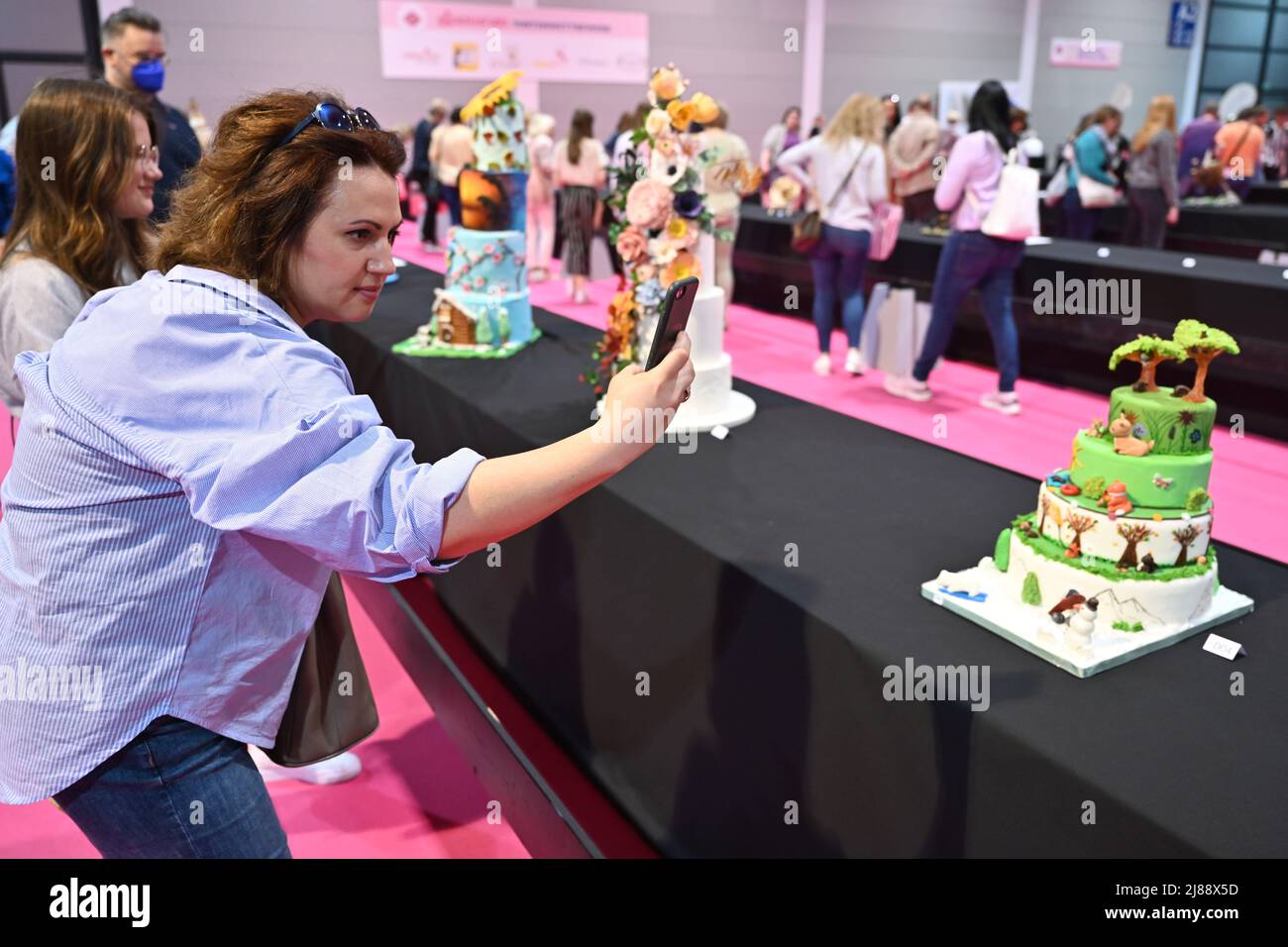 Friedrichshafen, Germania. 14th maggio 2022. Un visitatore scatta una foto di una torta multilivello con il suo telefono cellulare. Decine di torte insolite sono in mostra al 'My Cake 2022', la fiera internazionale per il design della torta e la cottura creativa. Credit: Felix Kästle/dpa/Alamy Live News Foto Stock