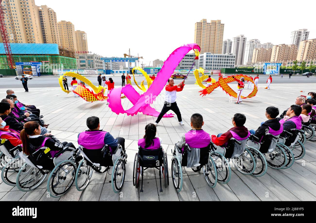 ZHANGYE, CINA - 14 MAGGIO 2022 - le persone disabili guardano una danza drago al Centro di lavoro assistito per disabili di Zhangye Jishanleye Foto Stock