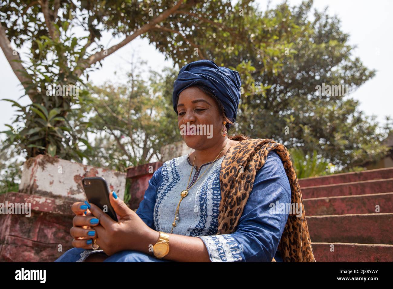 La donna africana vestita tradizionalmente usa il suo smartphone, la donna e il concetto di tecnologia Foto Stock