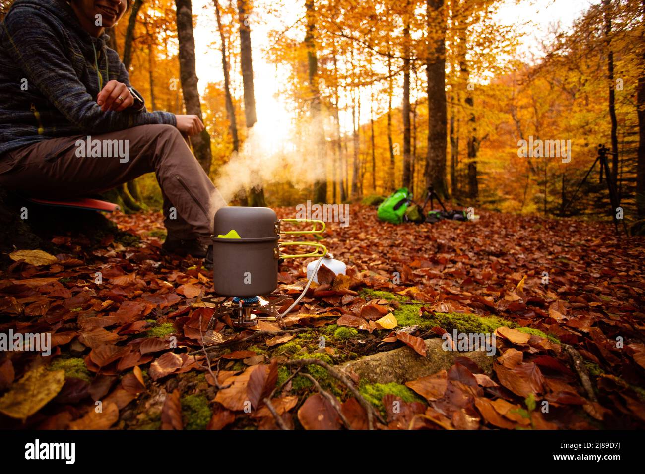 La donna usa un riscaldatore a gas portatile e una padella per cucinare all'aperto Foto Stock