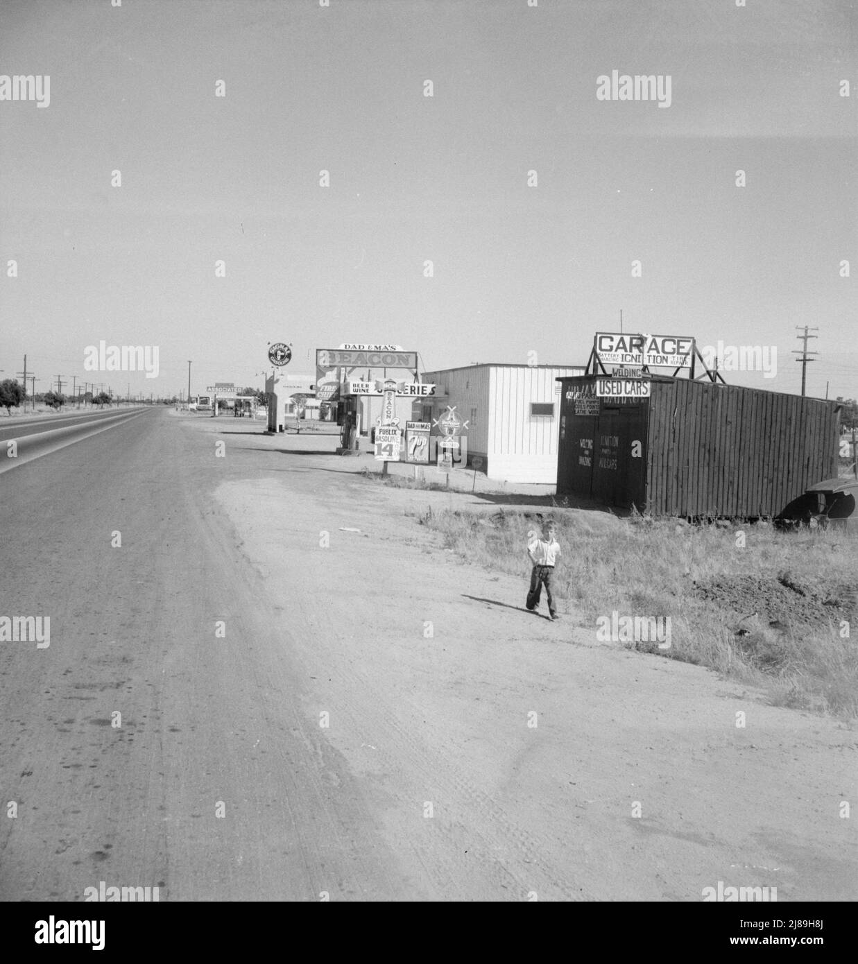 Tra Tulare e Fresno, California. Lungo l'autostrada US 99 a Highway City. [Segni che fanno pubblicità alla benzina; papà e amp; negozio di Ma's Beacon; birra, vino e generi alimentari; 7up; Dr Pepper; automobili usate; carica della batteria; saldatura; parti automatiche Foto Stock