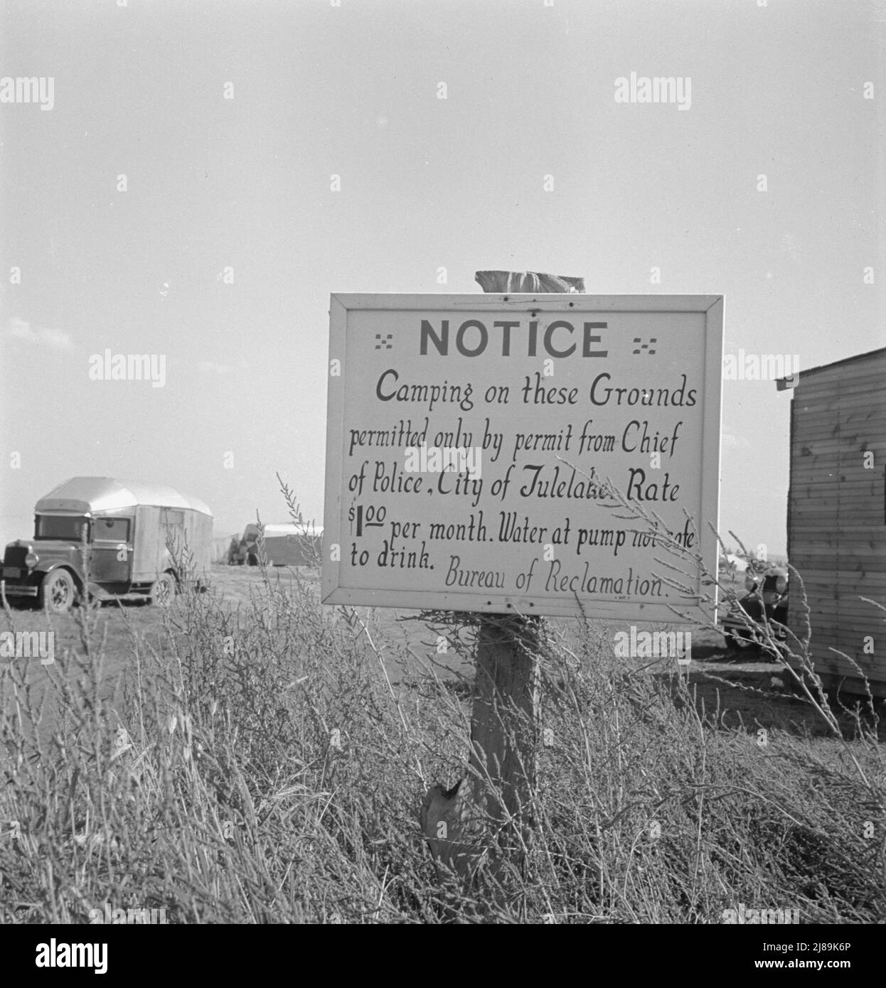 Cartello sul campo di fronte ai capannoni per l'imballaggio delle patate. Tulelake, contea di Siskiyou, California. ['avviso - Camping per questi motivi consentito solo da permesso del capo della polizia. Città di Tulelake. Tariffa $1,00 al mese. Acqua alla pompa non sicura da bere. Bureau of Reclamation"]. Foto Stock