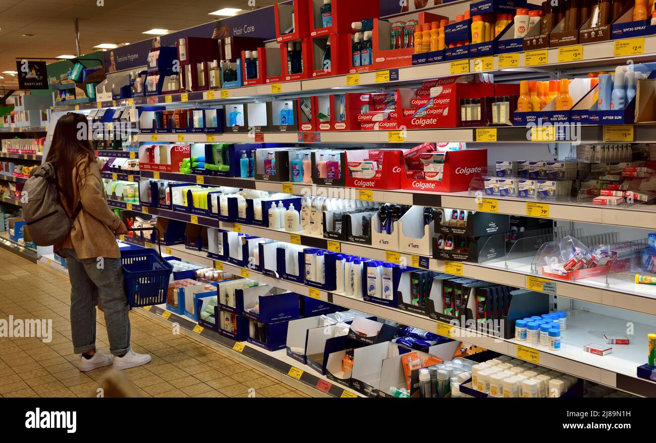 Donna che acquista con cestino nel corridoio di articoli domestici del supermercato di Aldi, Regno Unito Foto Stock