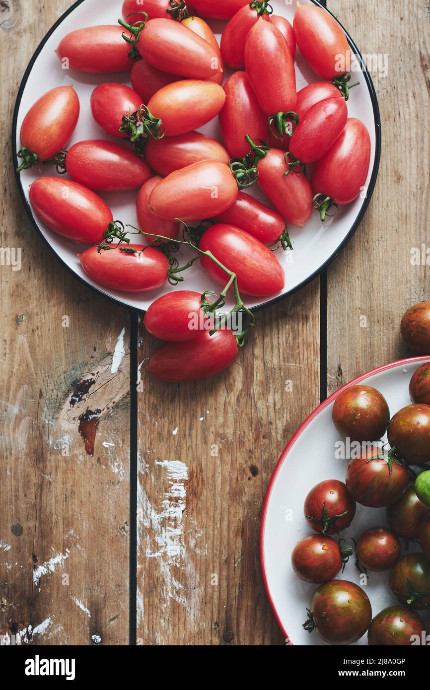Pomodori ciliegini rossi e neri su sfondo di legno. Foto Stock